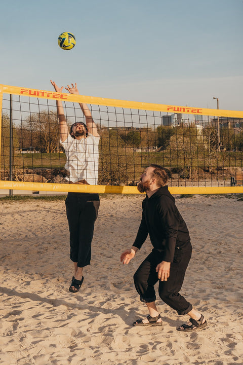 4. Two men playing volleyball on sand wearing Omaking Lauri Leather Sandals in black, ideal for outdoor activities