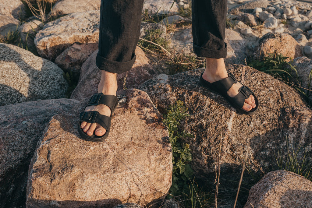 2. Men's black Märt Sandals by Omaking shown on rocks, highlighting leather upper and supportive insole