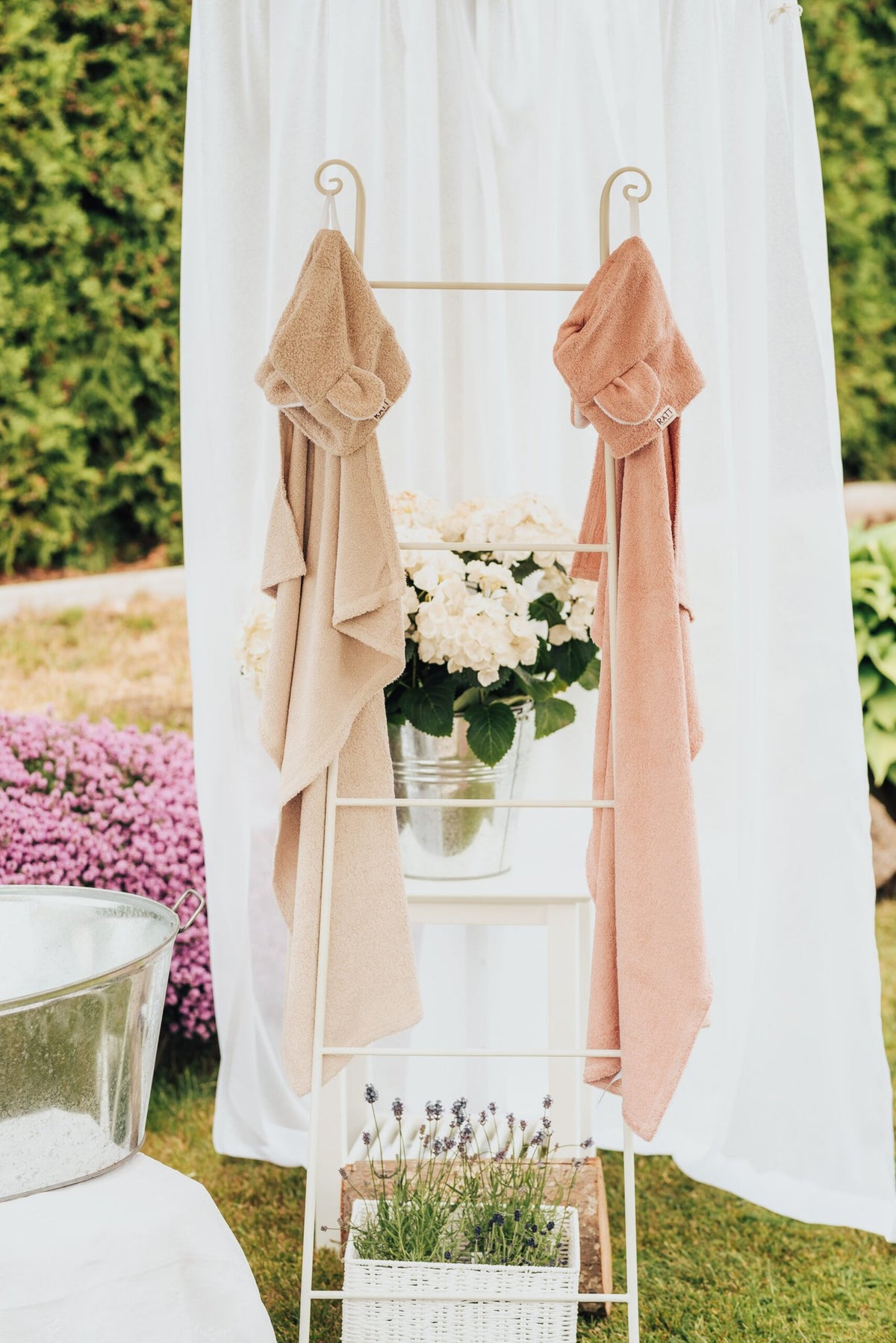 9. RÄTT hooded baby bath towels in beige and pink displayed on rack with flowers, outdoor setting