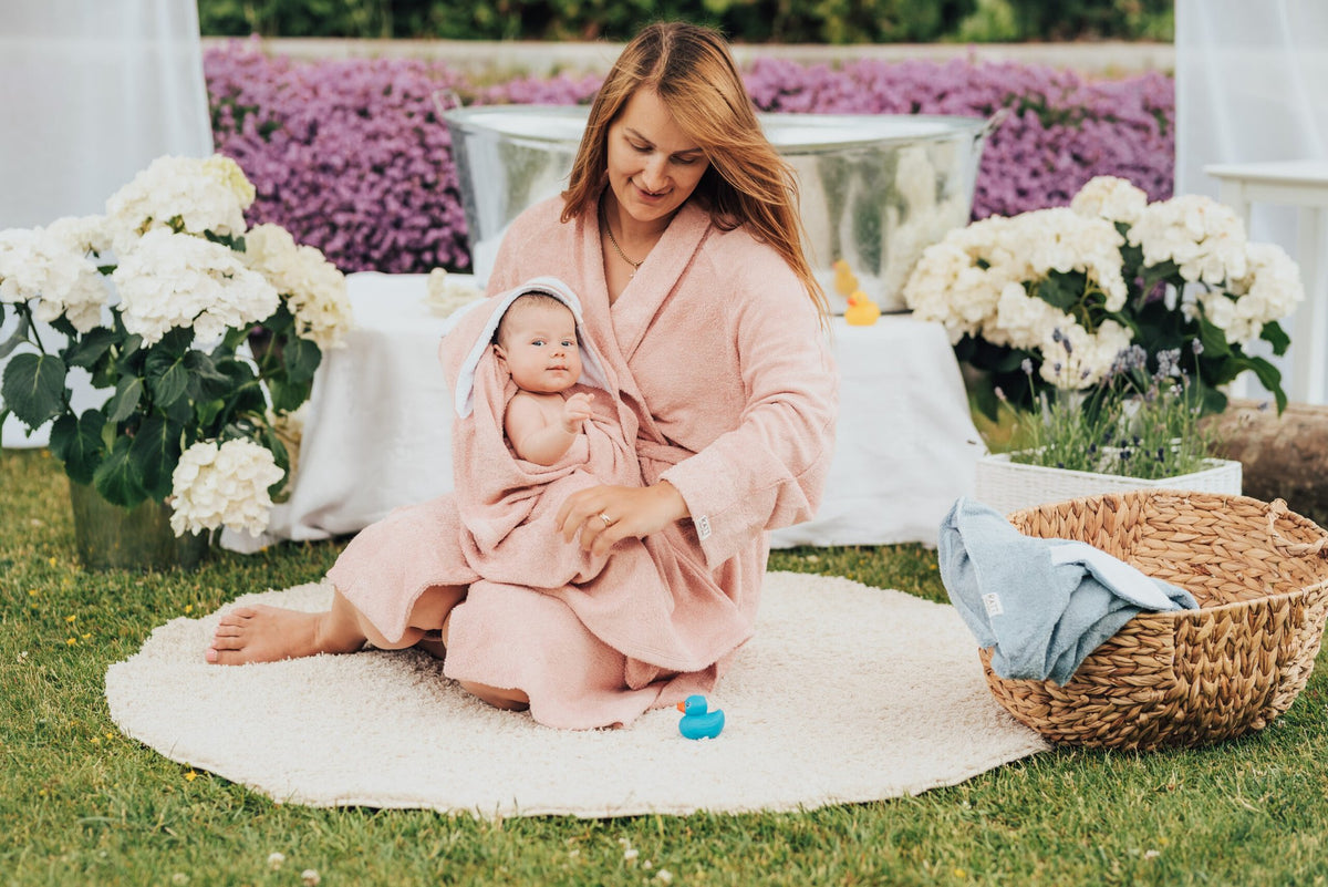 2. Mother sitting with baby wrapped in RÄTT Hooded Baby Bath Towel TEDDY, garden setting
