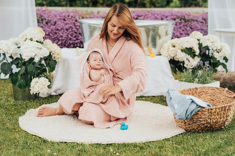 2. Mother sitting with baby wrapped in RÄTT hooded baby bath towel with rabbit ears, garden setting