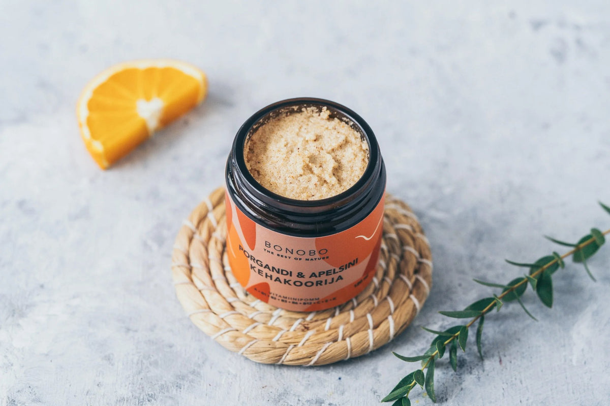 1. Open jar of BONOBO orange and carrot body scrub on woven mat with orange slice, showcasing texture