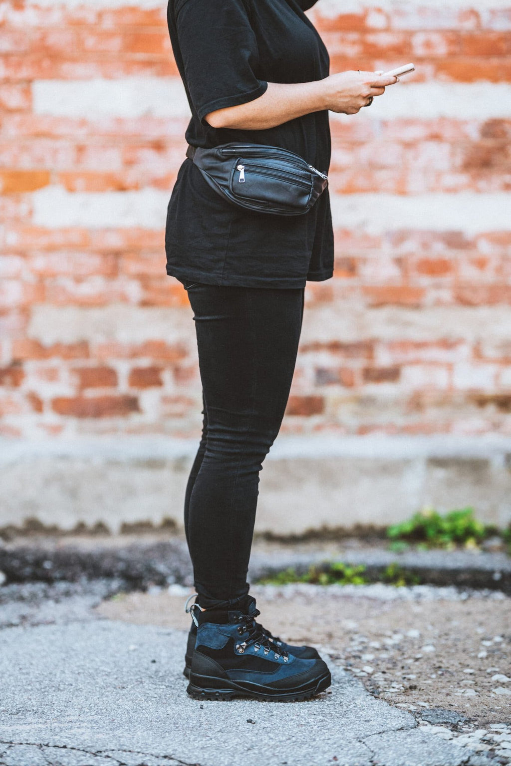 1. Woman wearing Papillon Leather Bum Bag No. 22 in black, styled with black outfit, shown in side view