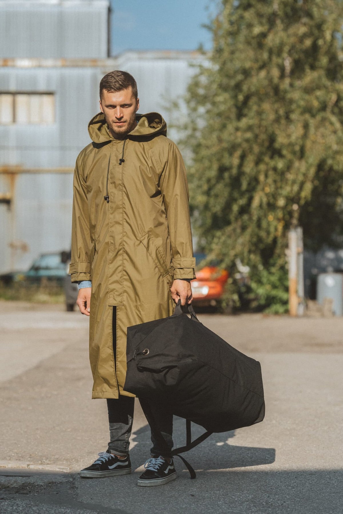 3. Men's Galvi Linda waterproof rain jacket in olive green, shown with matching black storage bag, highlighting outdoor setting