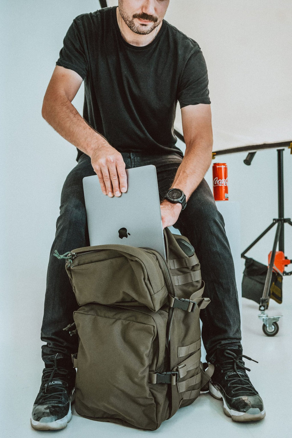 1. Man using Galvi-Linda Patrol Backpack 039 in military green, placing a laptop inside, studio setting