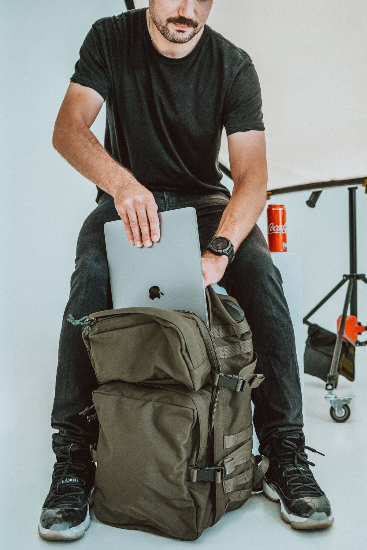 1. Man using Galvi-Linda Patrol Backpack 039 in military green, placing a laptop inside, studio setting