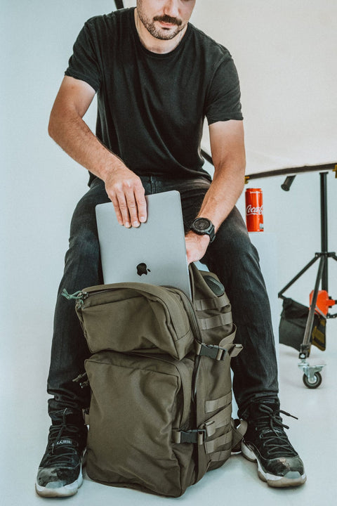 1. Man using Galvi-Linda Patrol Backpack 039 in military green, placing a laptop inside, studio setting