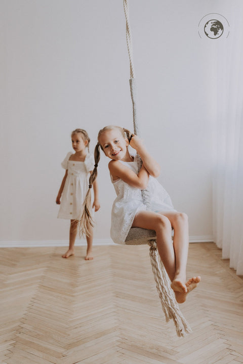 2. Two girls in white dresses playing with Nofi KIDS HopOn Swing in bright room, one sitting on swing