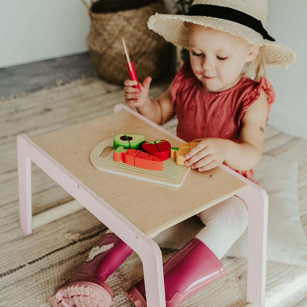 1. Young girl in pink dress and hat playing with toy food on small wooden desk in cozy room