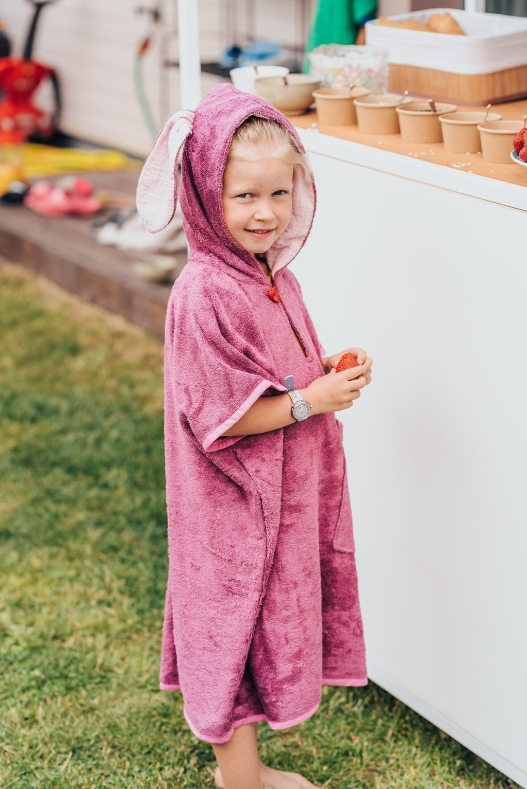 5. Child wearing pink RÄTT short-sleeve poncho with hood, standing outdoors