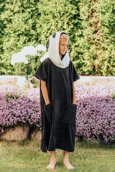 3. Child wearing RÄTT Short-Sleeve Poncho PANDA, standing in garden with hood up