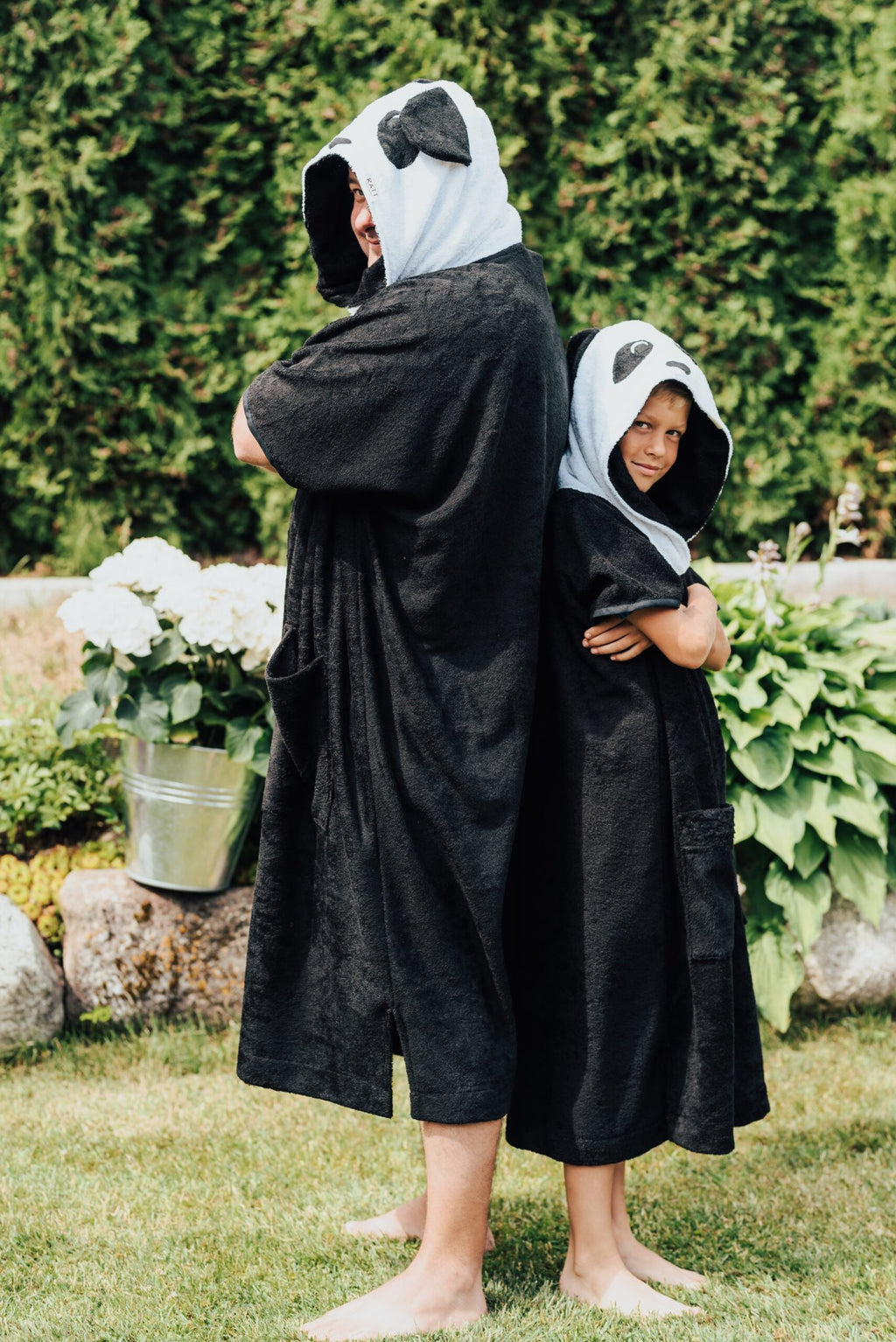 1. Child wearing RÄTT Short-Sleeve Poncho PANDA in garden setting, showcasing hood and pockets