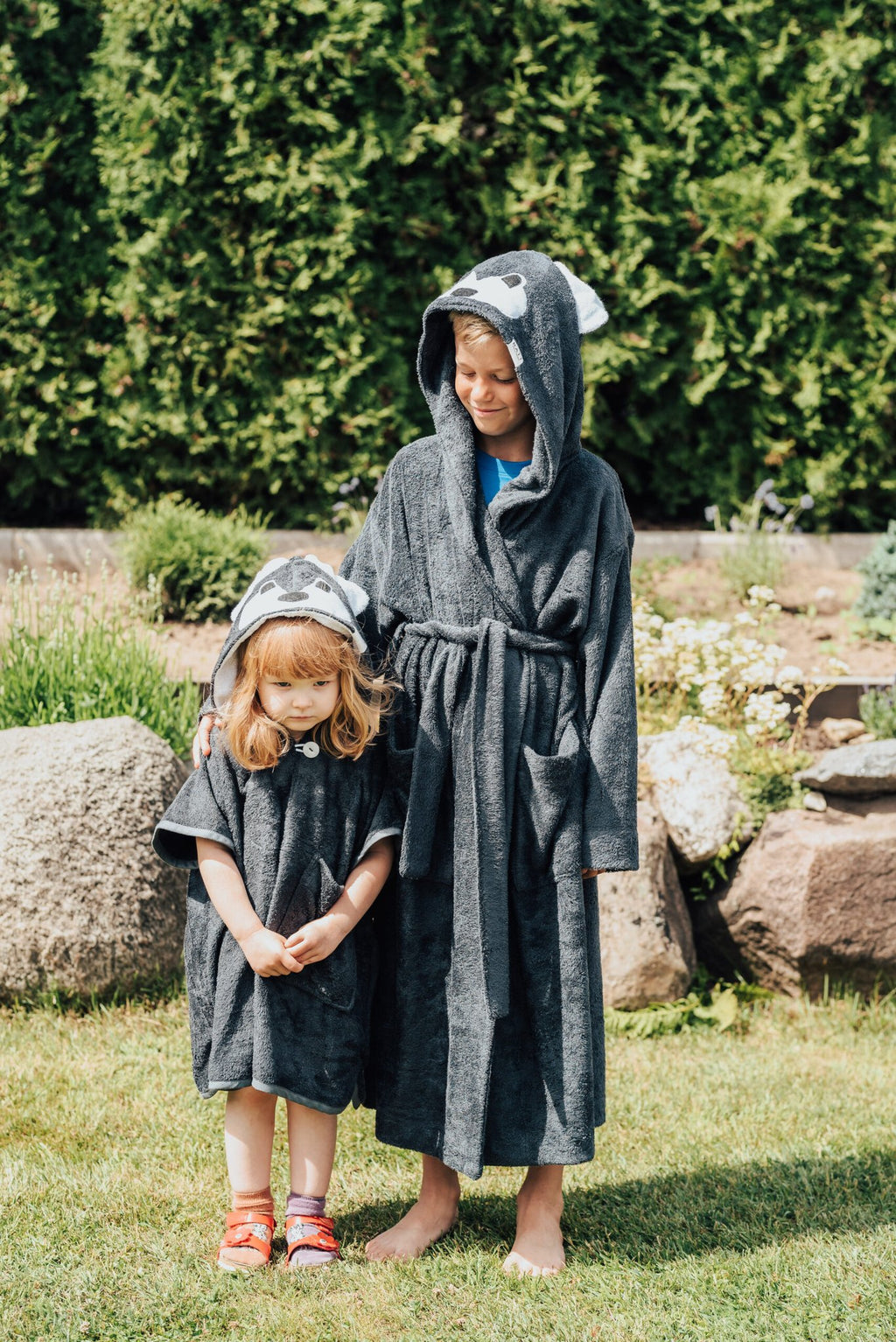 1. Two children wearing RÄTT WOLF Bamboo Terry Bathrobe for kids, featuring cozy hoods and belts, in a garden setting