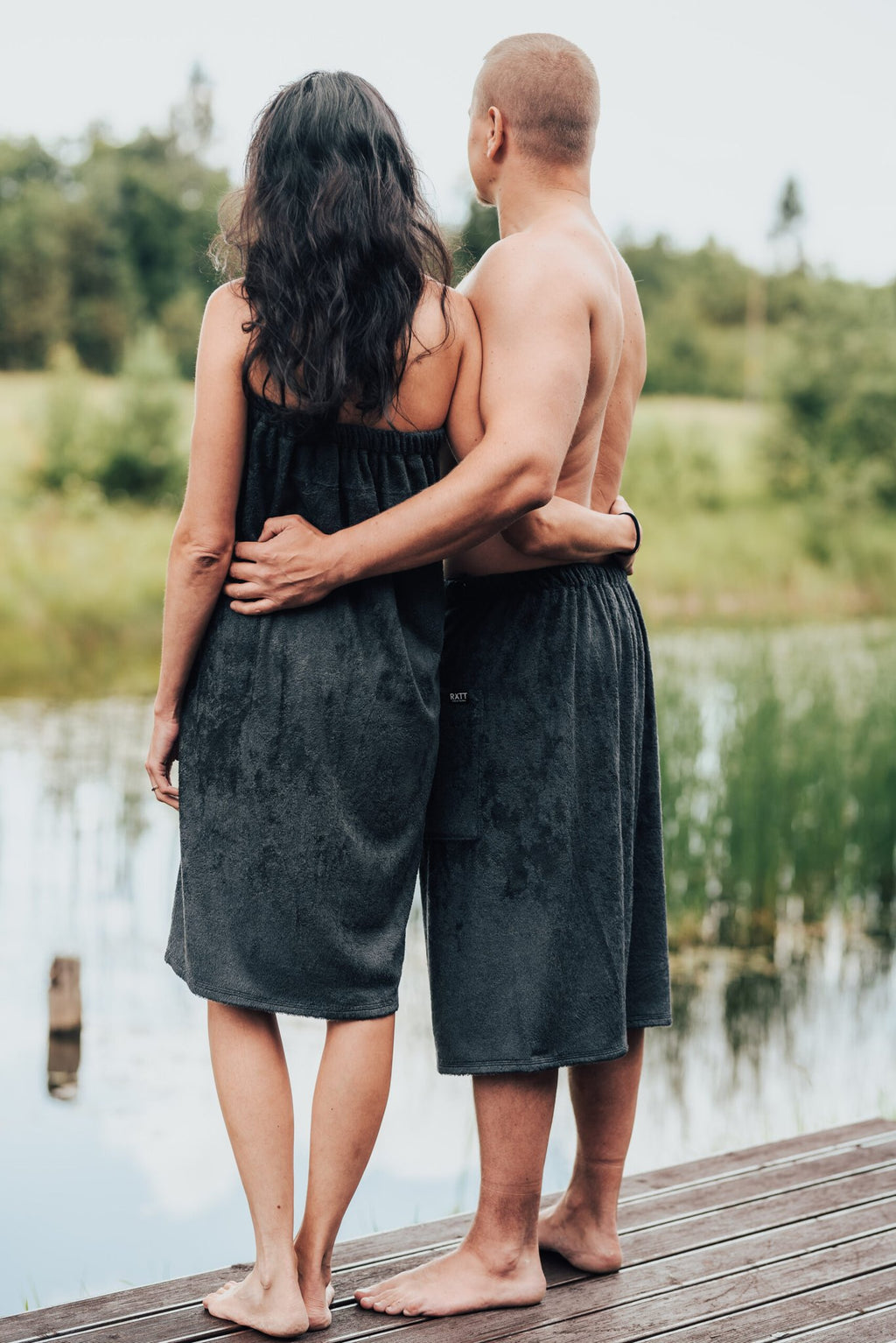 2. Back view of men's dark grey bamboo terry spa wrap by RÄTT, worn by male and female models near a pond