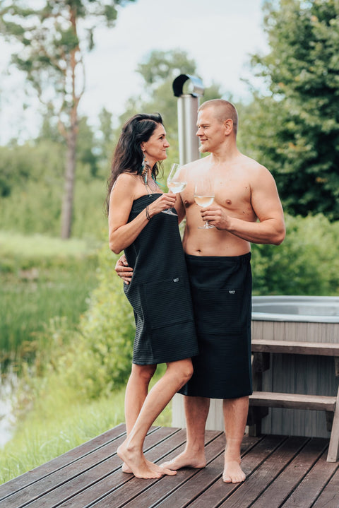 1. Men's black cotton waffle spa wrap by RÄTT, worn by male and female models outdoors, ideal for spa or sauna