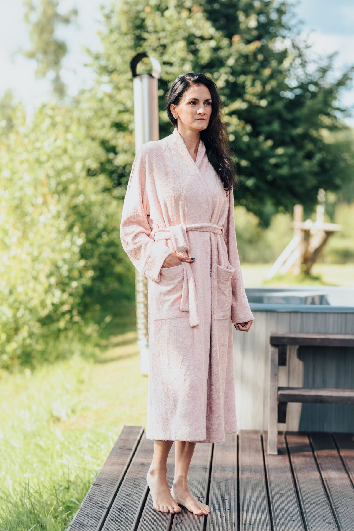 3. Woman in a pink bamboo terry bathrobe by RÄTT, standing on a wooden deck, emphasizing the robe's absorbent and skin-friendly fabric