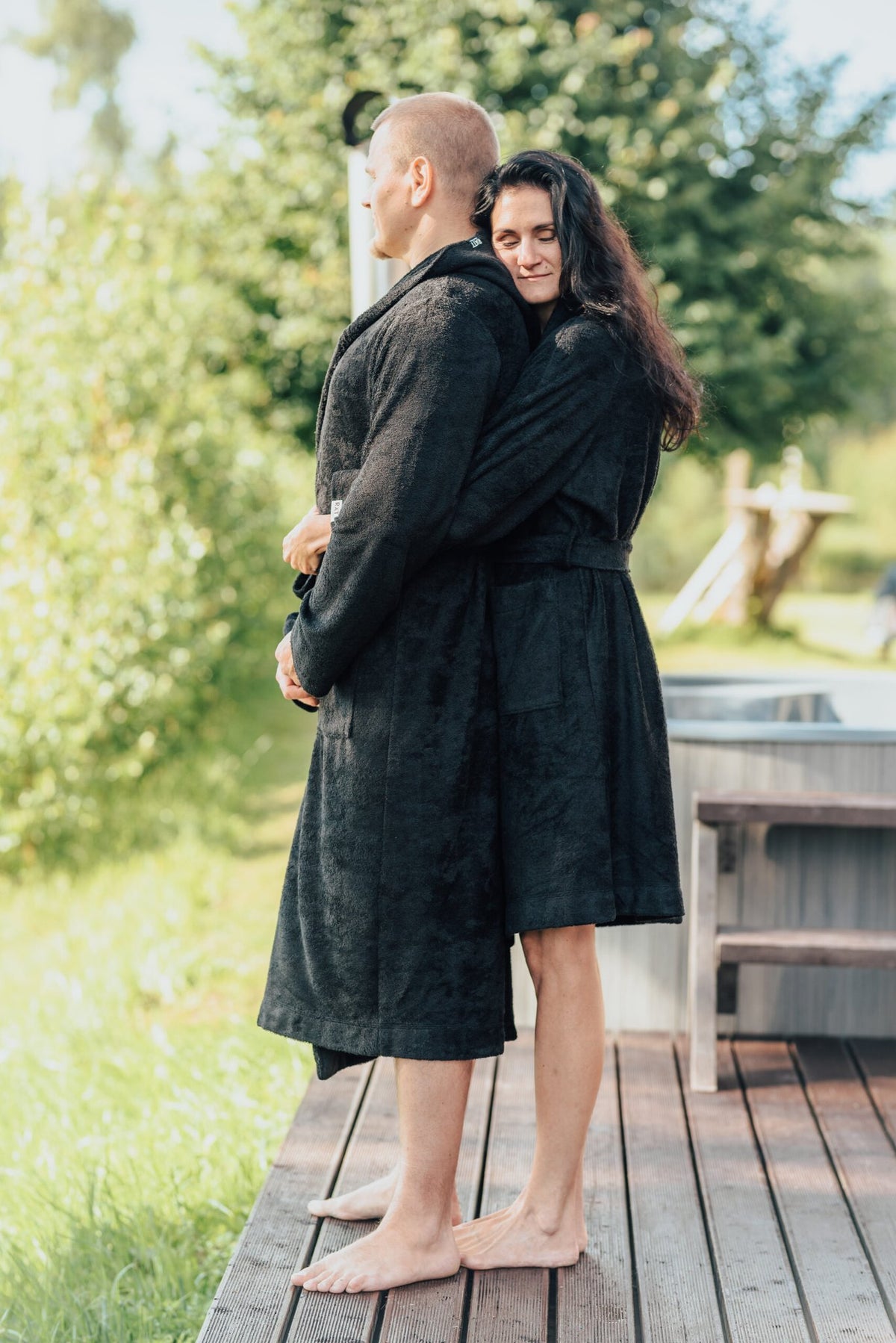 2. Unisex black bamboo terry bathrobes worn by a couple embracing outdoors, highlighting hooded design