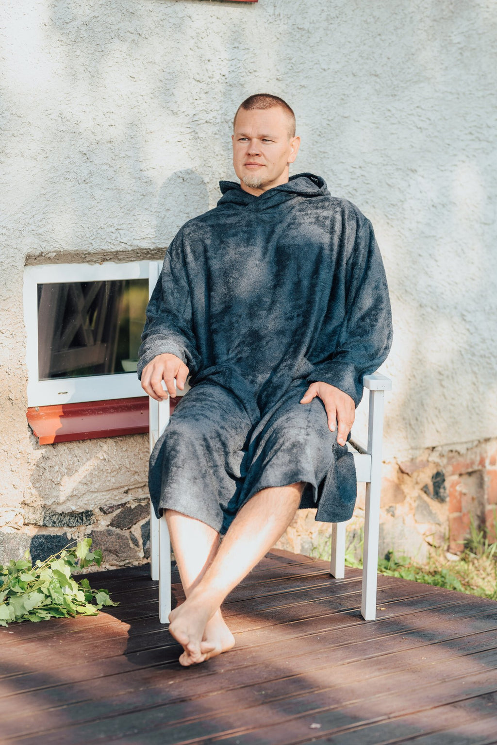 7. Men's dark gray bamboo terry long-sleeve poncho with hood, worn by model sitting on a chair outdoors