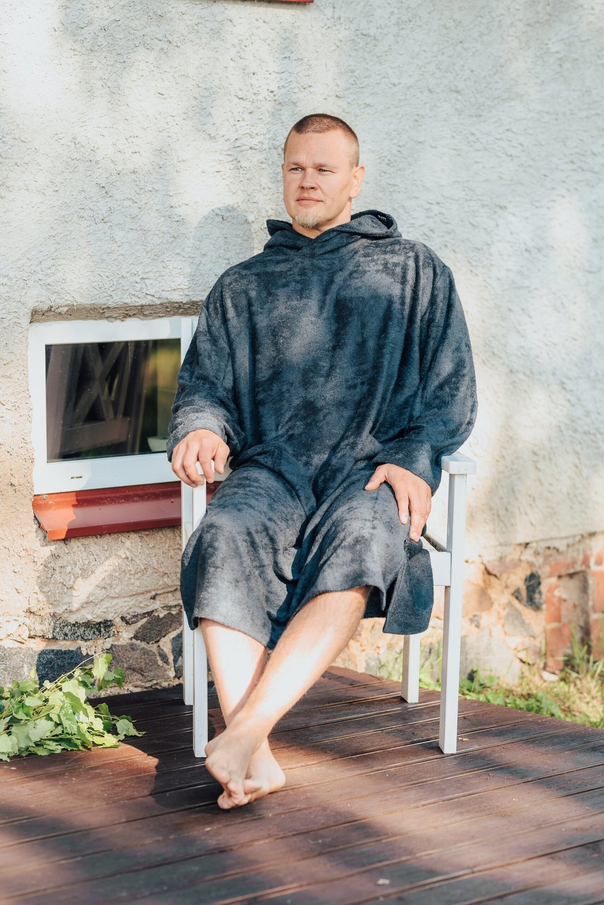 7. Men's dark gray bamboo terry long-sleeve poncho with hood, worn by model sitting on a chair outdoors