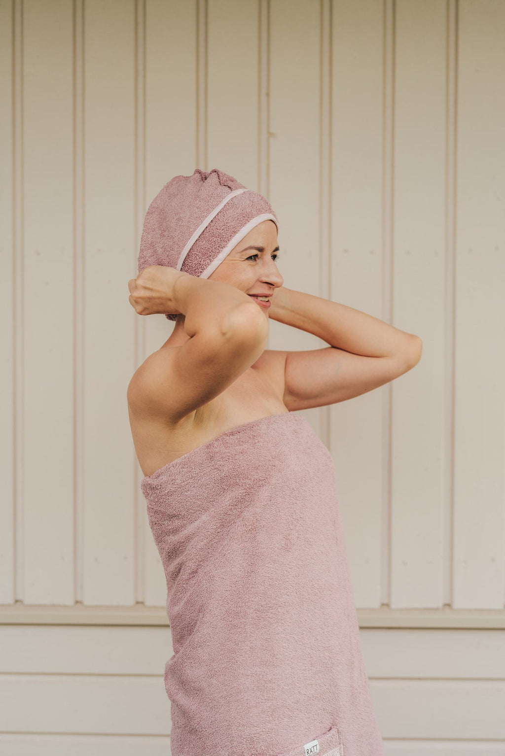 1. Woman adjusting RÄTT bamboo terry hair wrap in pink, demonstrating easy wear and comfort