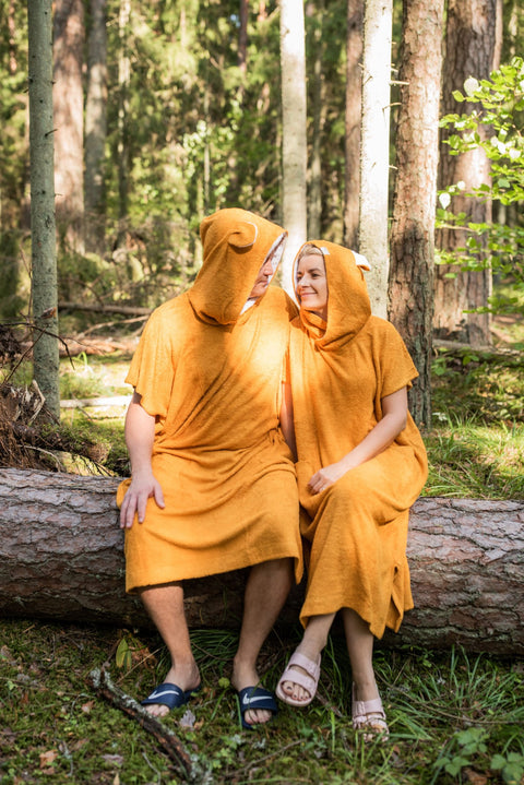 1. Unisex orange bamboo terry ponchos worn by male and female models sitting on a log in a forest