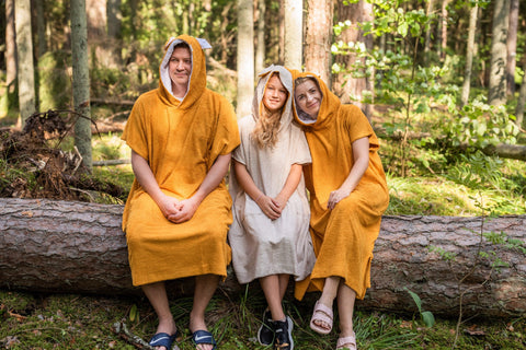 2. Unisex bamboo terry ponchos in orange and beige worn by three models sitting on a log in a forest