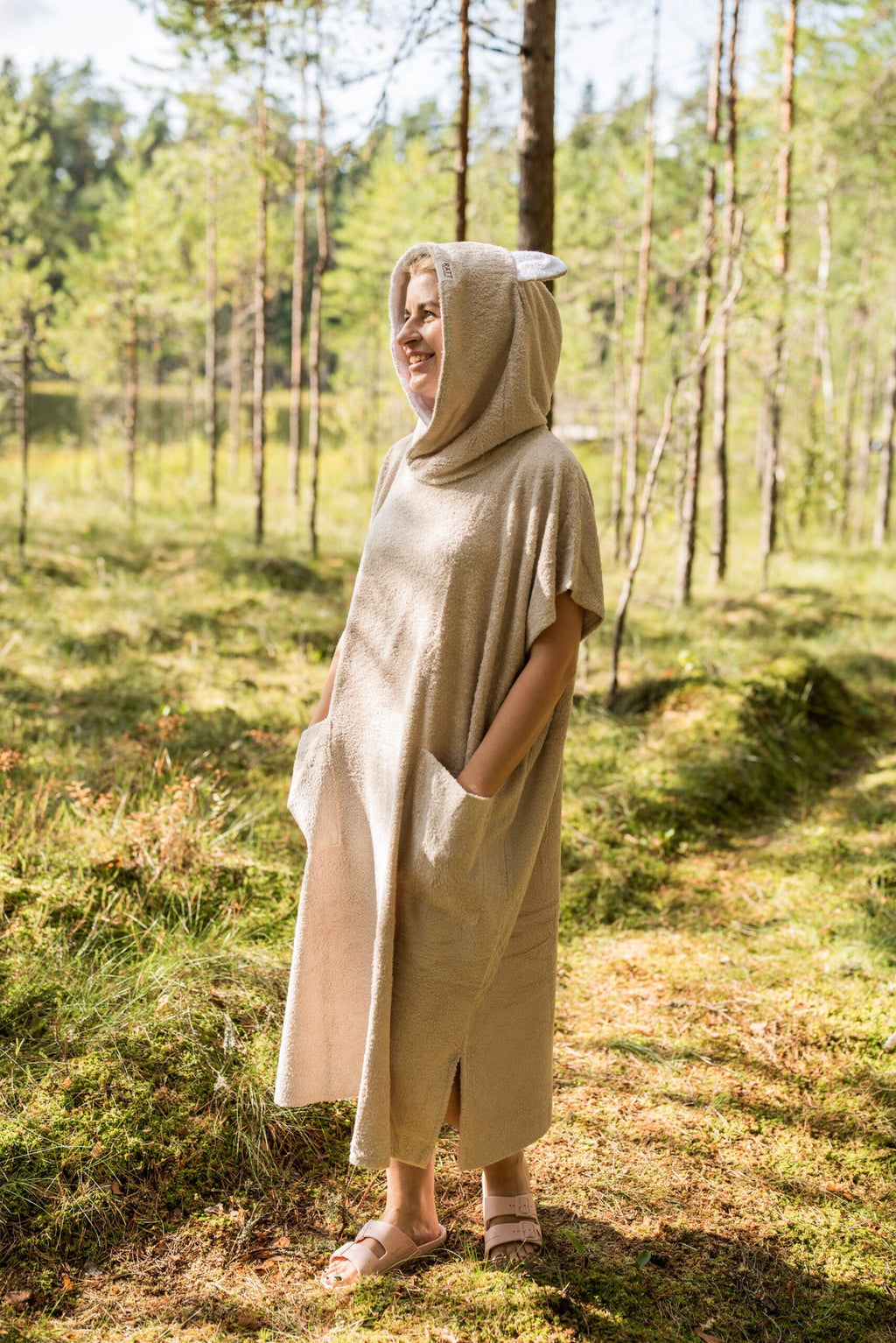 4. Woman wearing beige bamboo terry poncho with hood, standing in a forest setting