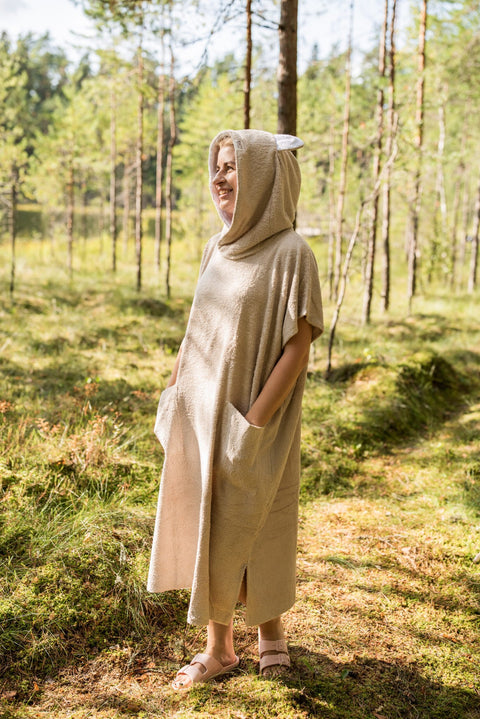 4. Woman wearing beige bamboo terry poncho with hood, standing in a forest setting