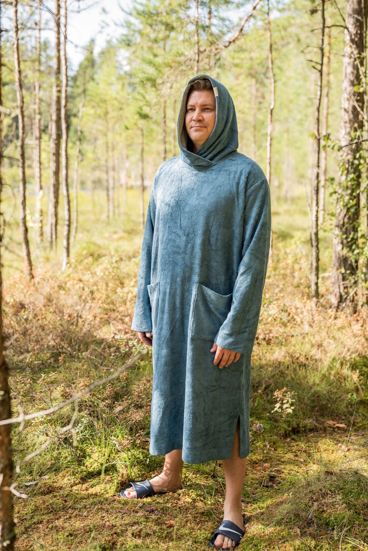 5. Men's blue bamboo terry long-sleeve poncho with hood, worn by model standing in a forest setting