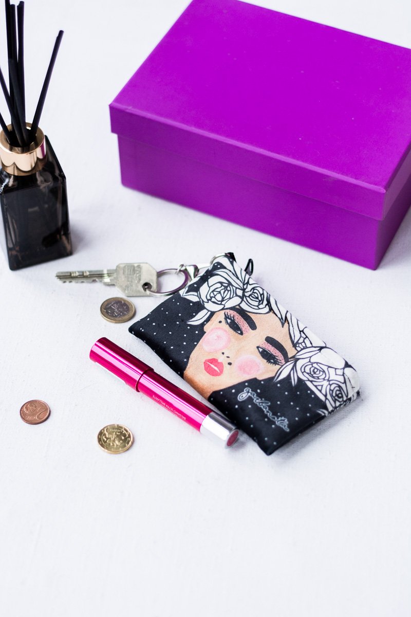4. Garbanota Key Pouch Yoko in black velour with artistic design, displayed with coins and lipstick next to a purple box