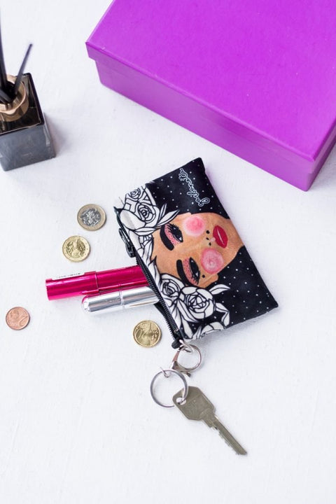 1. Garbanota Key Pouch Yoko in black velour with artistic face design, shown with coins and lipstick on a white surface