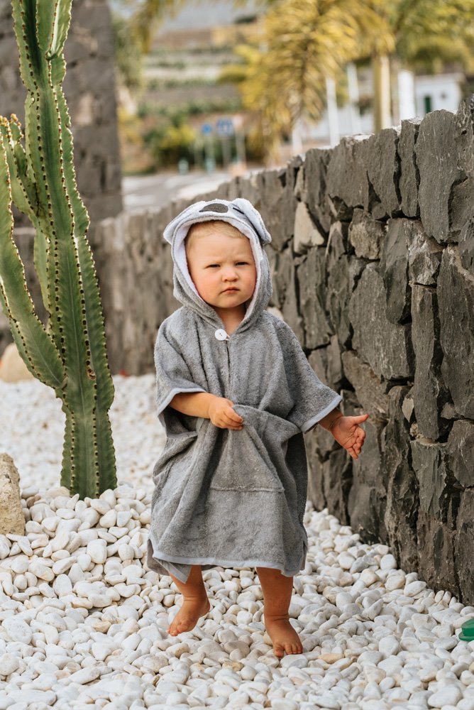 7. Toddler in grey RÄTT short-sleeve poncho with koala hood, standing on white stones