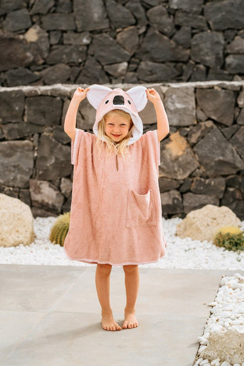 1. Child wearing pink RÄTT Short-Sleeve Poncho KOALA with hood, standing outdoors