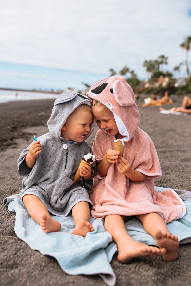 8. Two children sitting on beach in RÄTT Short-Sleeve Poncho KOALA, pink and gray