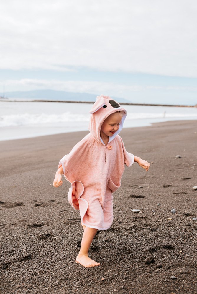 2. Toddler in pink RÄTT short-sleeve poncho running on the beach, showing hood and spacious cut
