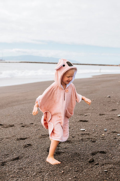 2. Toddler in pink RÄTT short-sleeve poncho running on the beach, showing hood and spacious cut