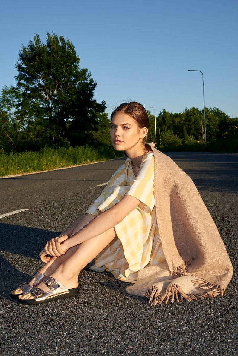 1. Woman wearing Omaking Meeliku Sandals in rose gold, sitting on a road in a summer dress