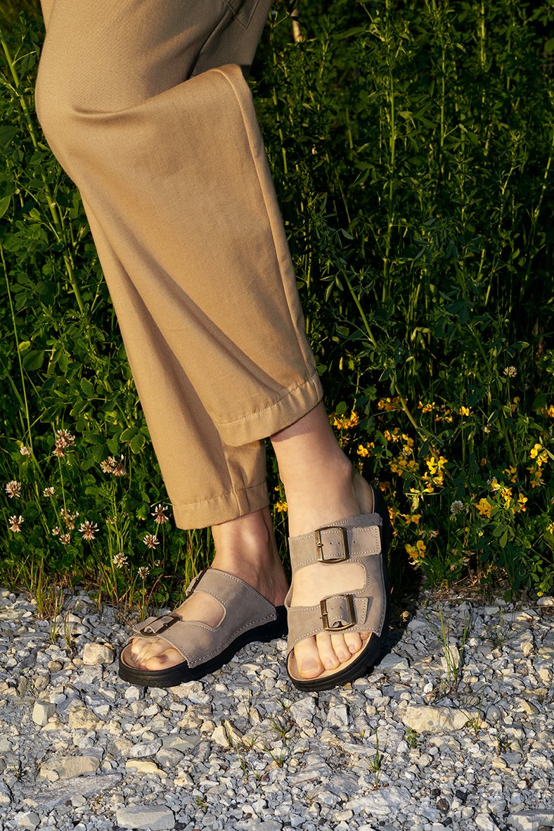 4. Close-up of Omaking Meeliku grey leather sandals worn by a woman, showing adjustable buckle straps and natural leather insole