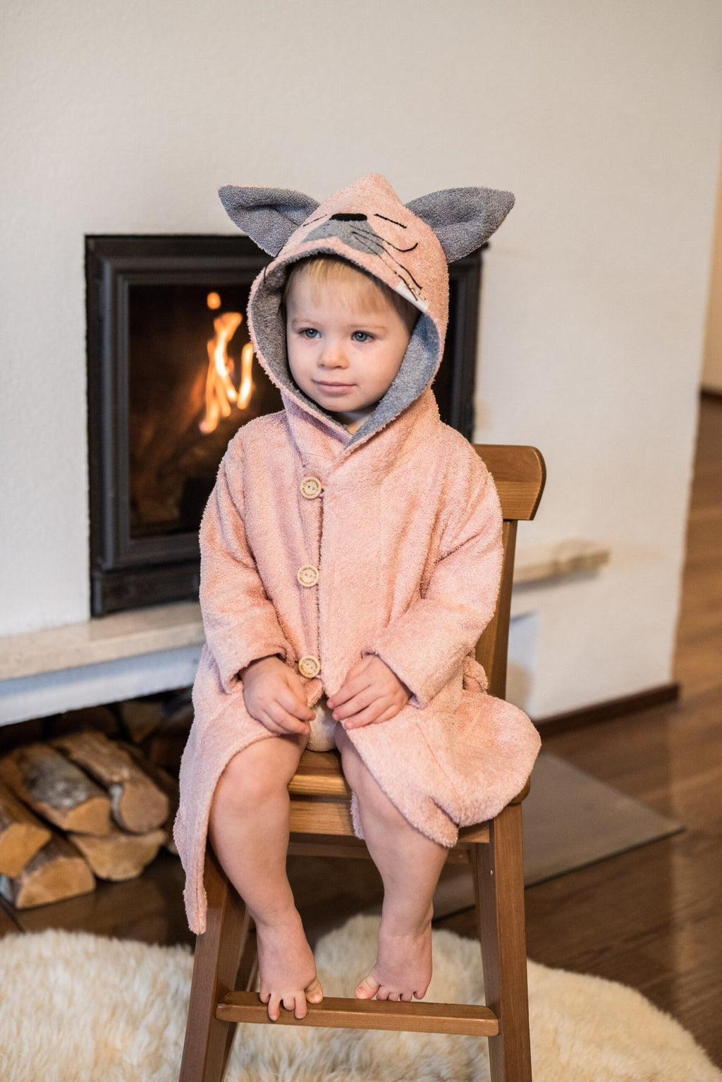 3. Toddler in pink RÄTT Bamboo Terry Bathrobe CAT with hood, sitting by fireplace
