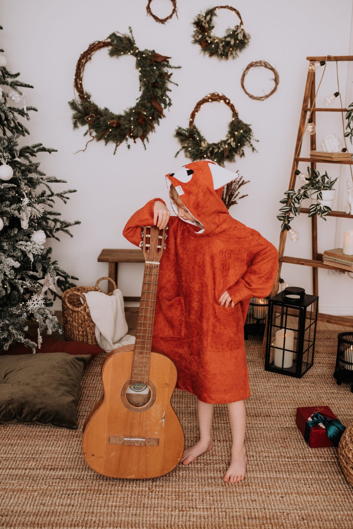 2. Child in RÄTT Long-Sleeve Poncho FOX, red color, posing with a guitar in a festive room