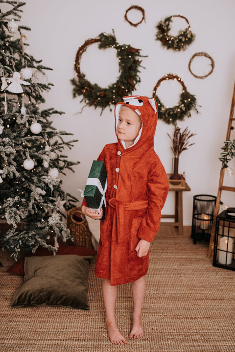 1. Child wearing RÄTT FOX Bamboo Terry Bathrobe in red with hood, shown in a cozy holiday setting
