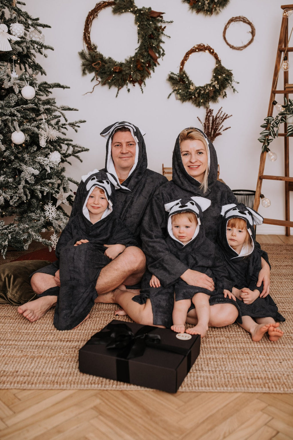 2. Family wearing matching RÄTT Long-Sleeve Poncho WOLF, showcasing children's and adult sizes, in a festive room