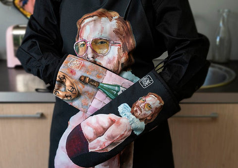 4. Person holding Katrin Valgemäe oven mitts with pop art design, including a portrait and 'Male Tears' bottle
