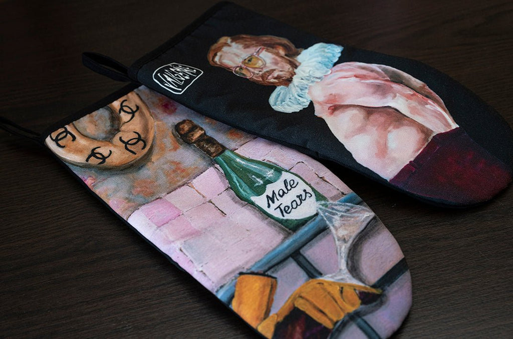 4. Flat lay of two Katrin Valgemäe oven mitts with pop art designs, including champagne bottle labeled 'Male Tears' and a man in ruff collar