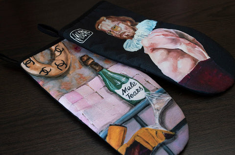 4. Flat lay of two Katrin Valgemäe oven mitts with pop art designs, including champagne bottle labeled 'Male Tears' and a man in ruff collar