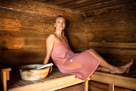 2. Woman in pink RÄTT spa wrap relaxing in a sauna, highlighting waffle fabric texture