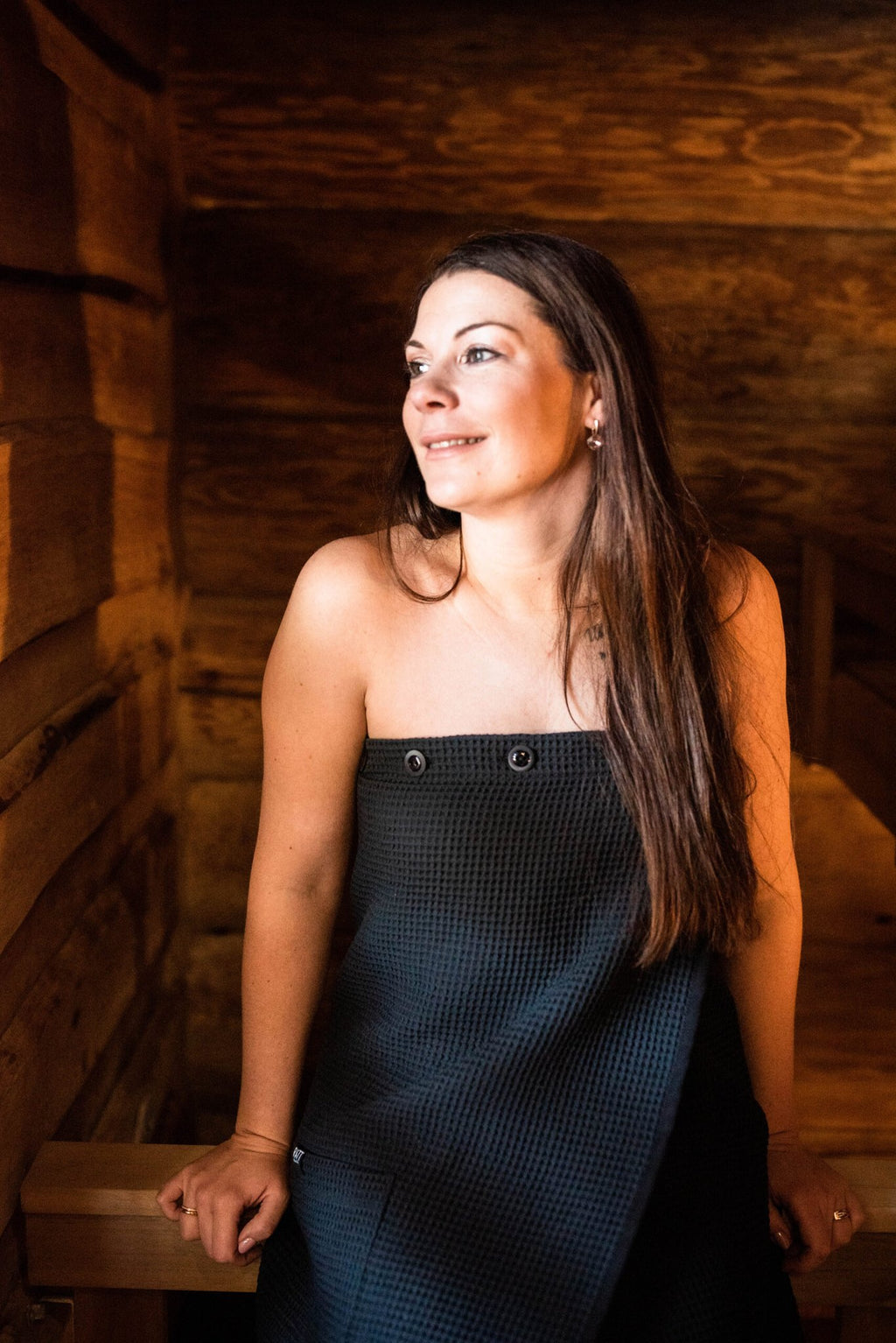 8. Woman in black RÄTT spa wrap in sauna, showcasing button detail and fit