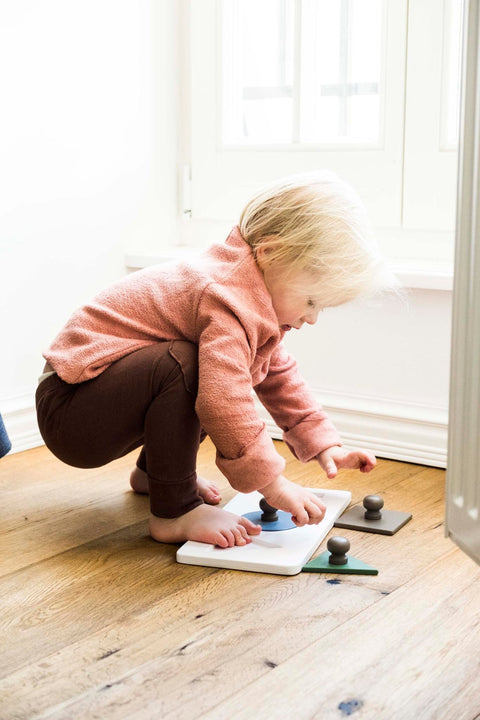 1. Child playing with Karloova Montessori wood shape puzzle on wooden floor, focusing on placing shapes into correct slots