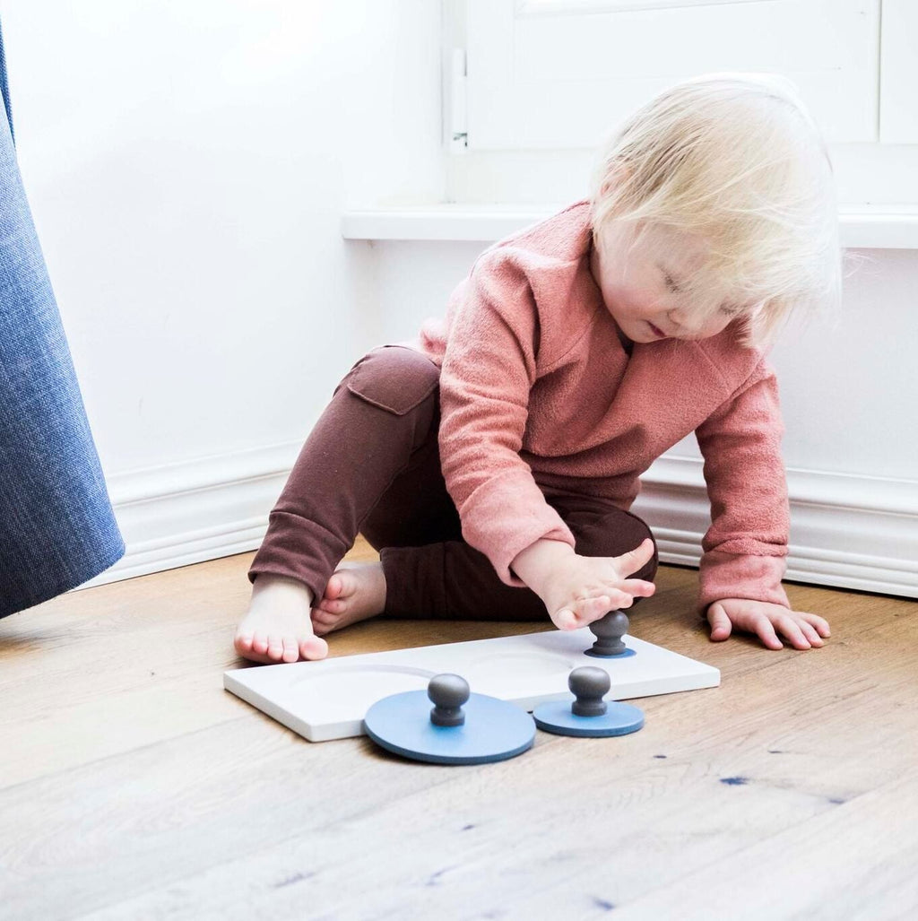 1. Child playing with Karloova solid wood Montessori shape puzzle on wooden floor, wearing pink top and brown pants