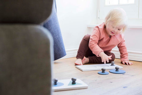 2. Child engaging with Karloova Montessori wood puzzle on floor, wearing pink top and brown pants, next to blue curtain